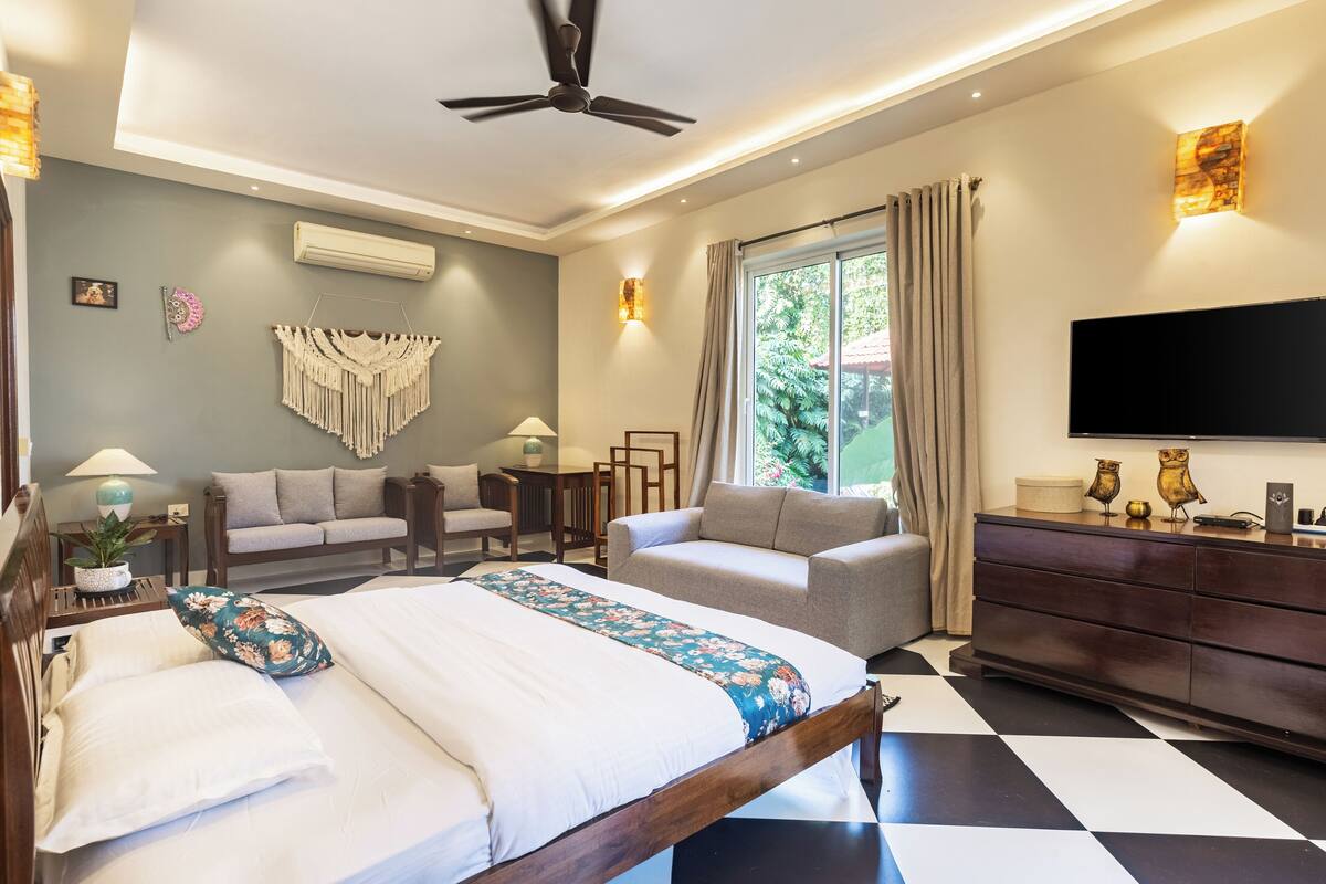 A modern hotel room with a bed, two sofas, a TV, and a large window.