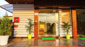 Entrada de hotel con fachada de madera, puertas de cristal y plantas en macetas.