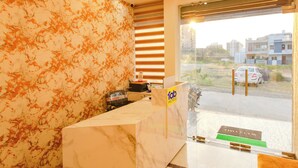 Zona de recepción de un hotel con mostrador de mármol, escritorio y vista al área de estacionamiento exterior.