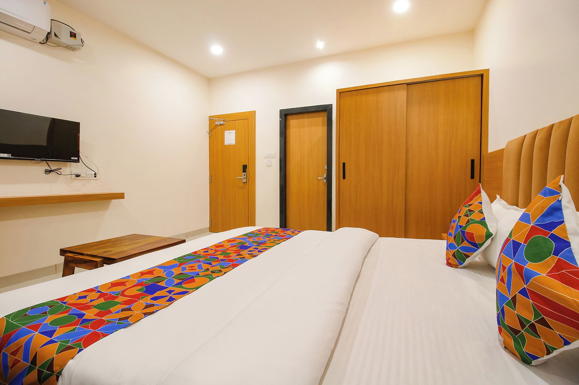 Une chambre d’hôtel avec un lit, un téléviseur fixé au mur et deux portes en bois.