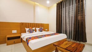 Una habitación de hotel con cabecera de madera, una cama con almohadas geométricas coloridas, una mesita de noche y una ventana con cortinas oscuras.