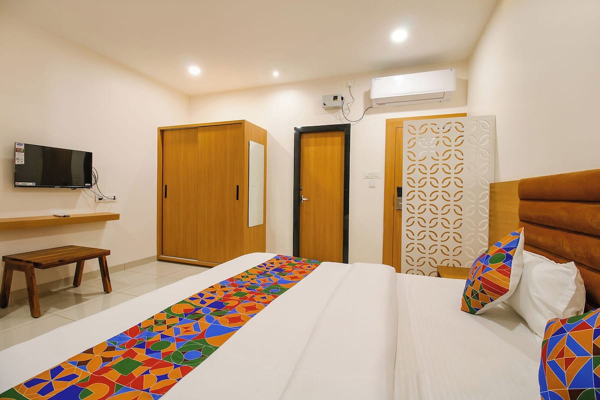 A hotel room with a bed, a TV, a wardrobe, a small table, and a decorative panel.