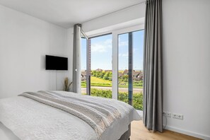 Une chambre dotée d’un grand lit, d’un téléviseur à écran plat et offrant une vue sur un paysage verdoyant grâce à de grandes fenêtres du sol au plafond.