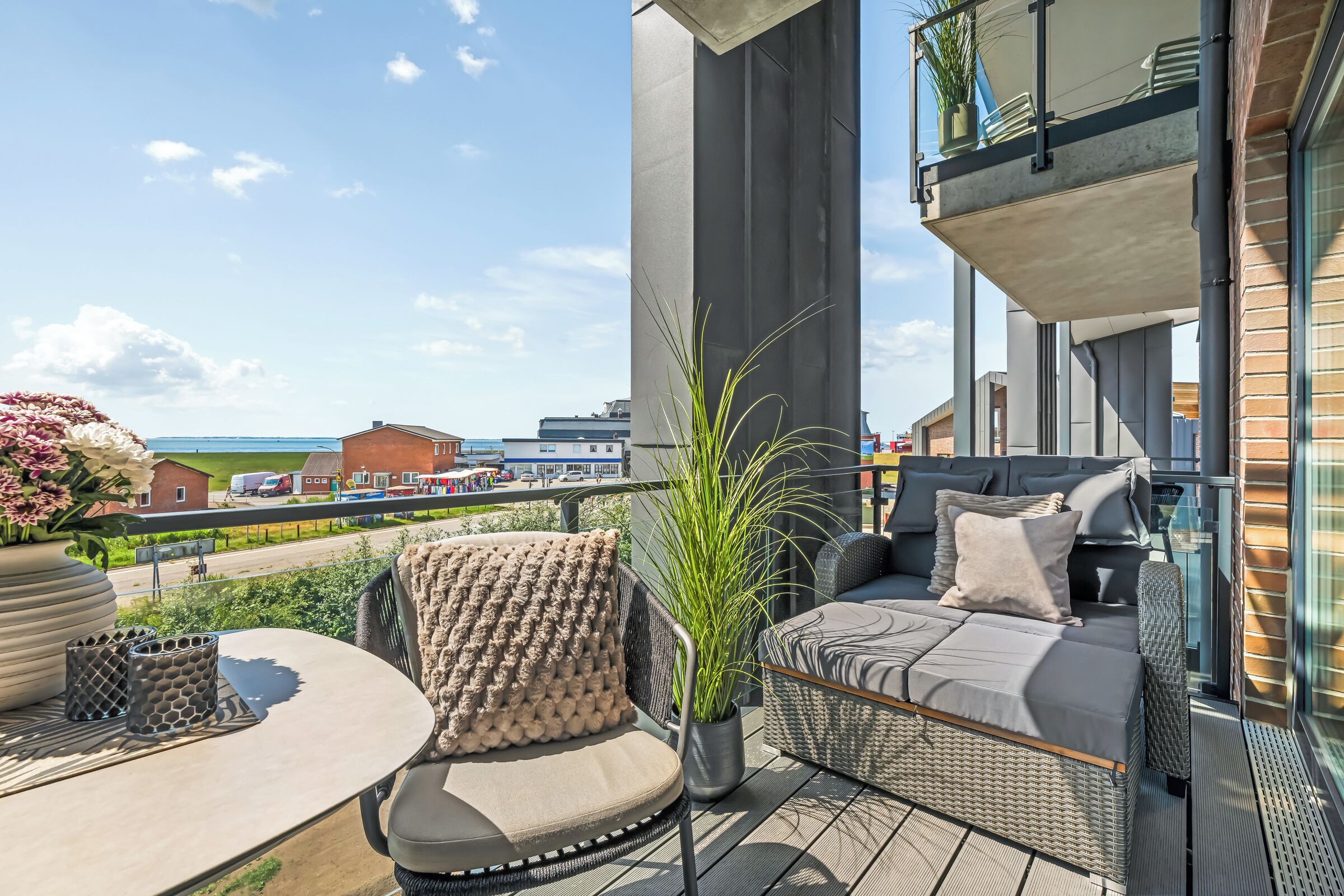 A balcony with outdoor furniture, a potted plant, and a view of the sea and buildings.