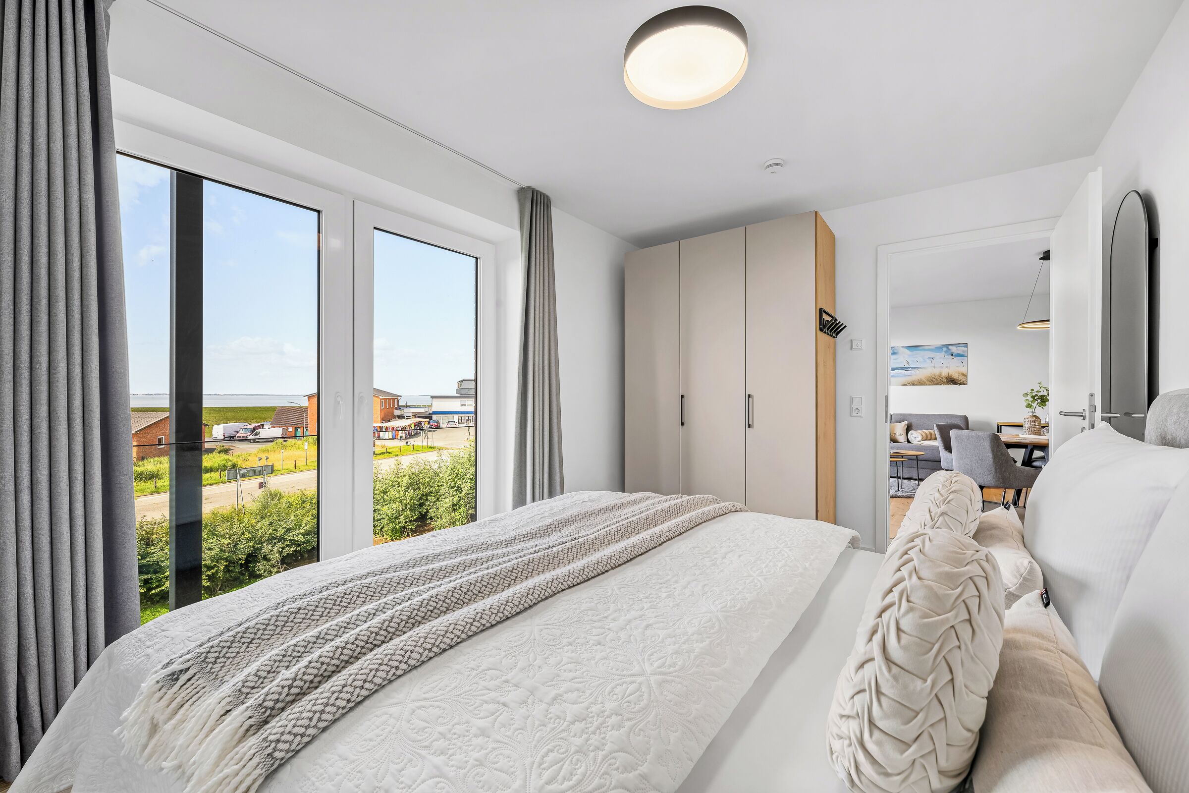 Ein modernes Schlafzimmer mit einem großen Bett, einem Kleiderschrank und Blick ins Freie.