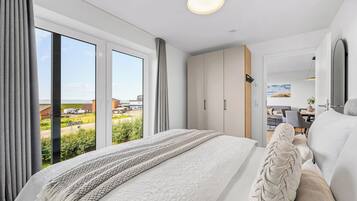 Ein modernes Schlafzimmer mit einem großen Bett, einem Kleiderschrank und Blick ins Freie.