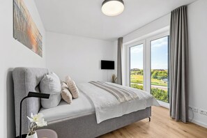 Ein modernes Schlafzimmer mit einem Bett, einem Flachbildfernseher und einem großen Fenster mit Blick ins Freie.