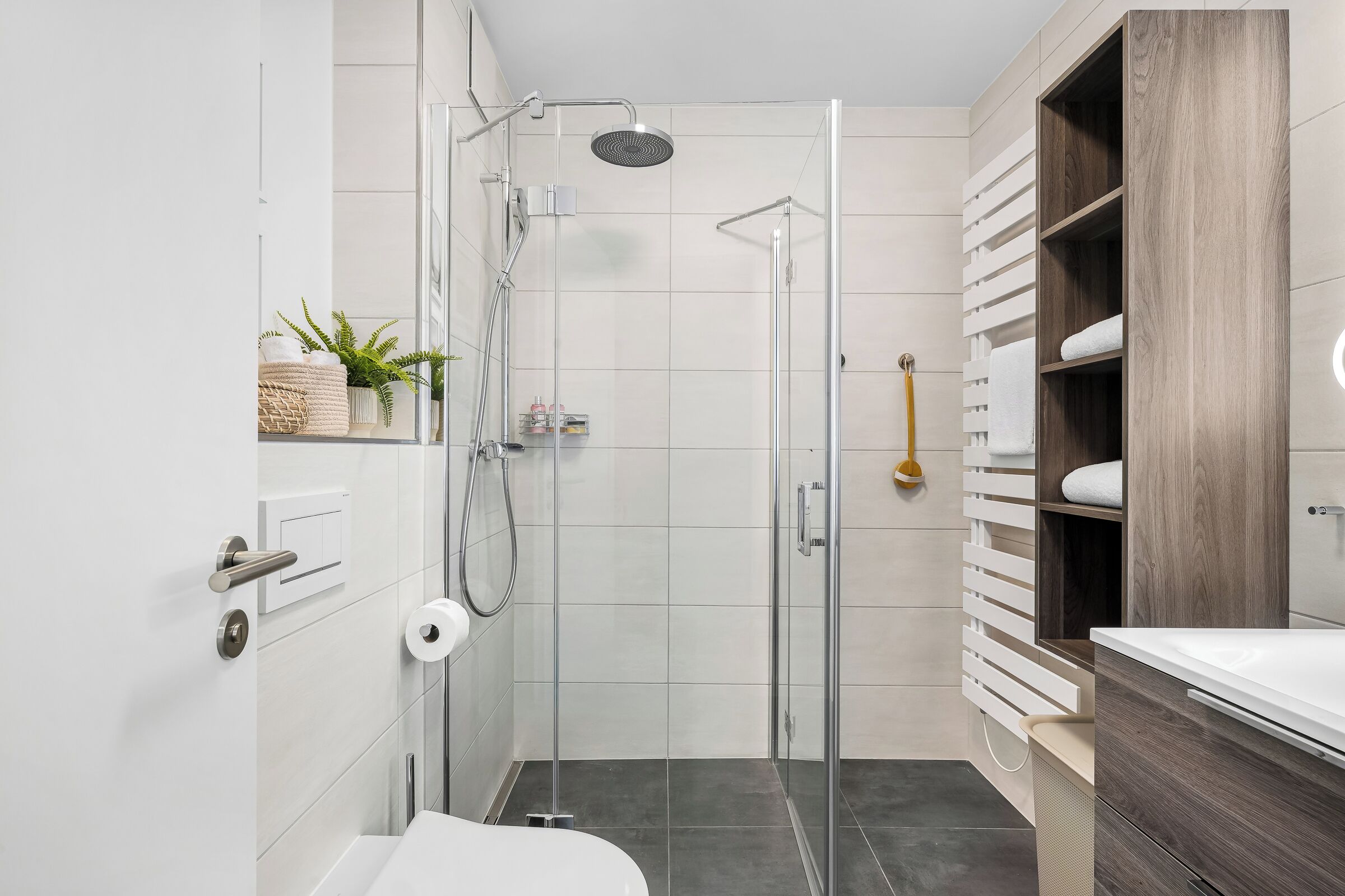 Ein modernes Badezimmer mit einer Duschkabine aus Glas, einem weißen Waschbecken und einem Holz-Waschtisch.