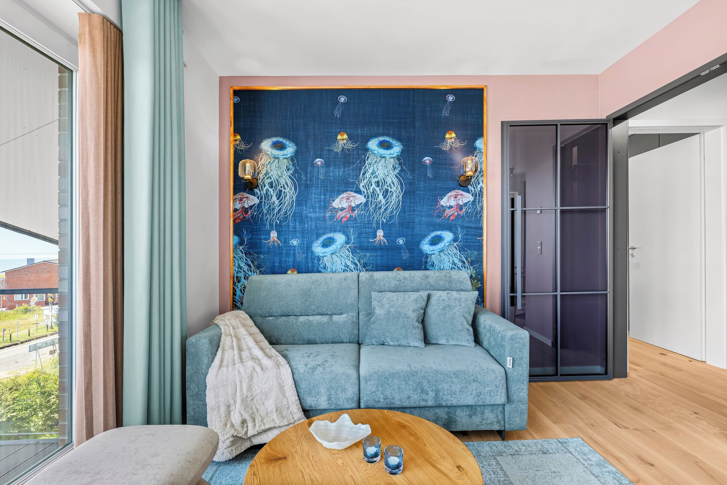 Ein modernes Wohnzimmer mit einem blauen Sofa, einem runden Holztisch und einer Wandtextilien mit Quallenmotiven.