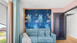 Uma sala de estar moderna com um sofá azul, uma mesa de centro redonda de madeira e um tapete na parede com desenhos de águas-vivas.