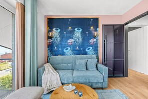 A modern living room with a blue sofa, a round wooden coffee table, and a tapestry with jellyfish designs on the wall. - The View B17 Boje 17 - Sea view, Sauna, shared. Washing machine,parking space (Dagebüll)