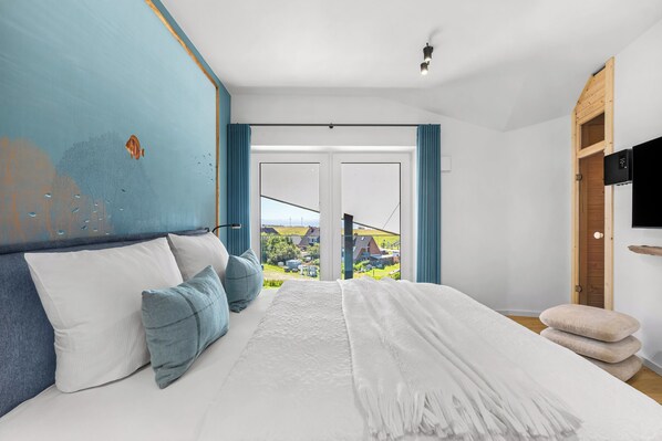 A bedroom with a large bed, a view of a residential area, and a wooden wardrobe.