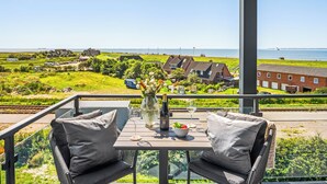Varanda com mesa posta para dois, com vista para a paisagem costeira com casas e um corpo de água.