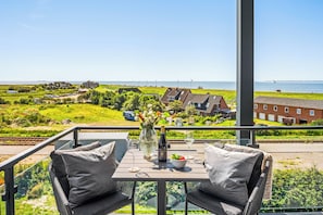 A balcony with a table set for two, overlooking a coastal landscape with houses and a body of water. - The View B17 Boje 17 - Sea view, Sauna, shared. Washing machine,parking space (Dagebüll)