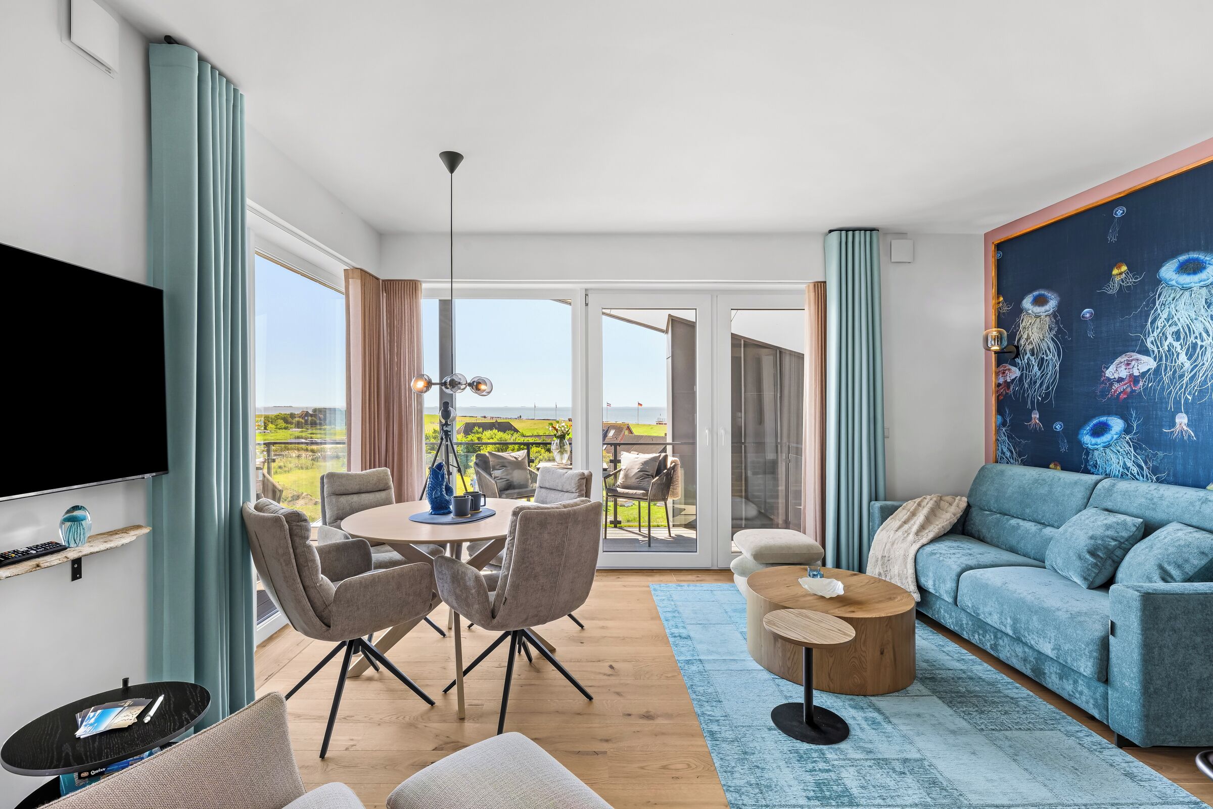 Ein modernes Wohnzimmer mit Flachbildfernseher, Essbereich mit Stühlen, einer Couch und einem großen Fenster mit Blick ins Freie.