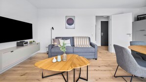 Een moderne woonkamer met een flatscreen televisie, een grijze bank, een houten salontafel en een grijze fauteuil.