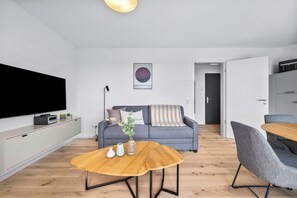 Ein modernes Wohnzimmer mit Fernseher, einem grauen Sofa, einem Holztisch und einem grauen Sessel.