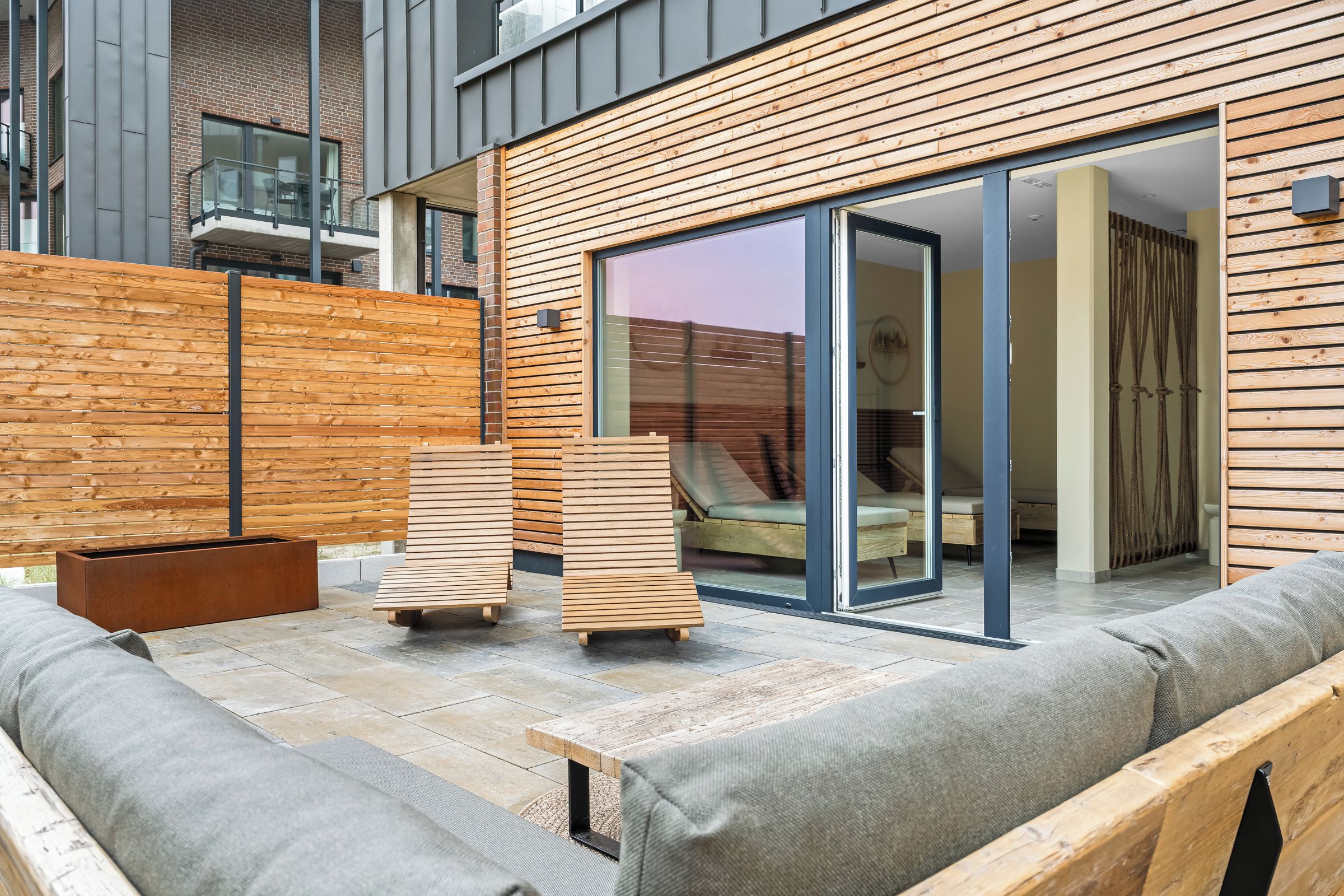 A modern outdoor seating area with a wooden deck, a built-in bench, and a glass door leading to a room.