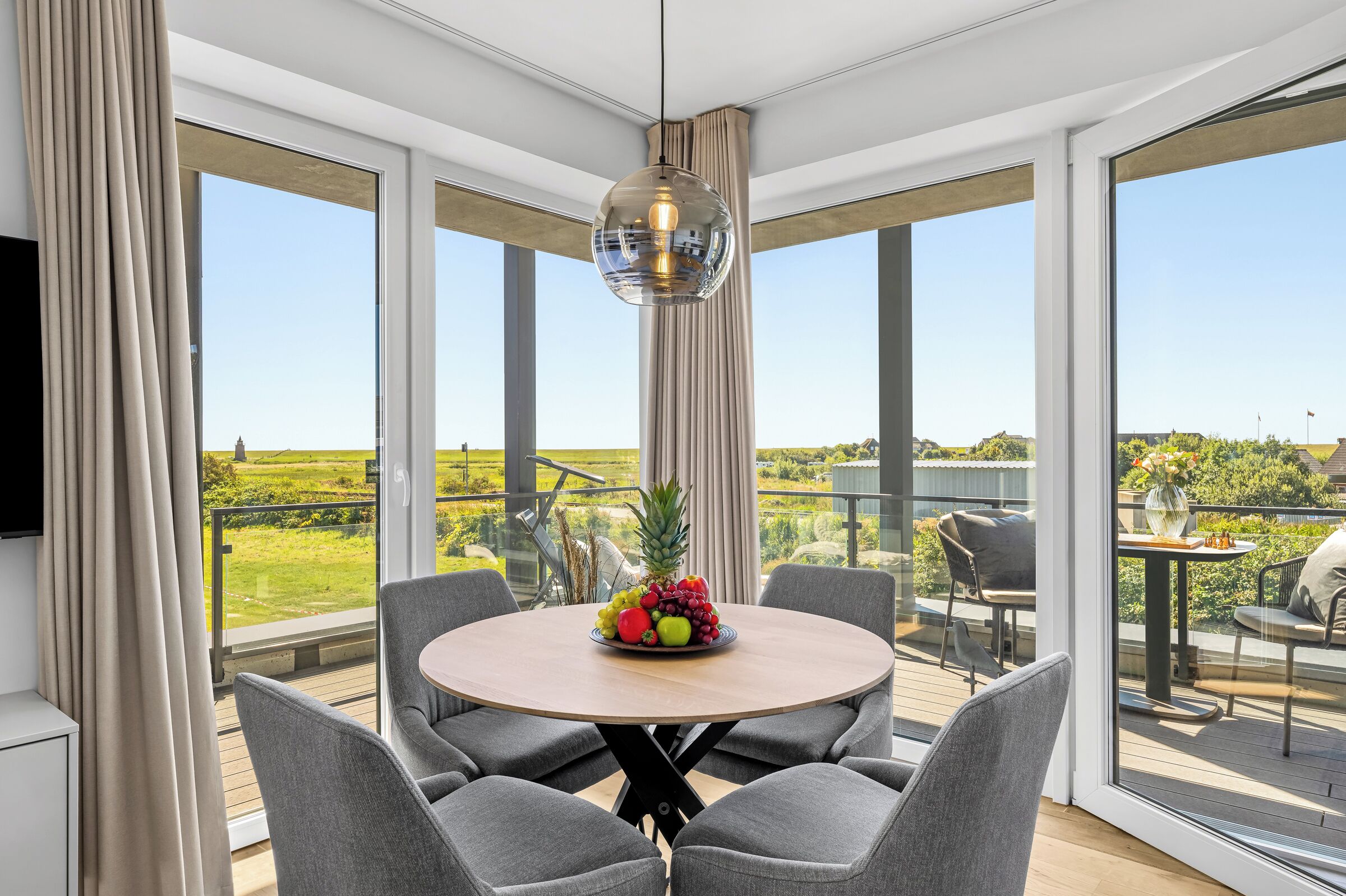 Een moderne eetruimte met een ronde tafel, gestoffeerde grijze stoelen en een hangende centraal geplaatste lamp.