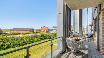 Een balkon met een schaakspel en stoelen, met uitzicht op een gazon en gebouwen.