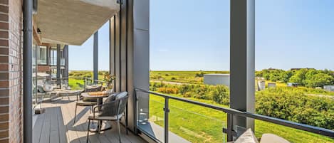 A balcony with outdoor furniture, a chessboard, and a view of a green landscape.