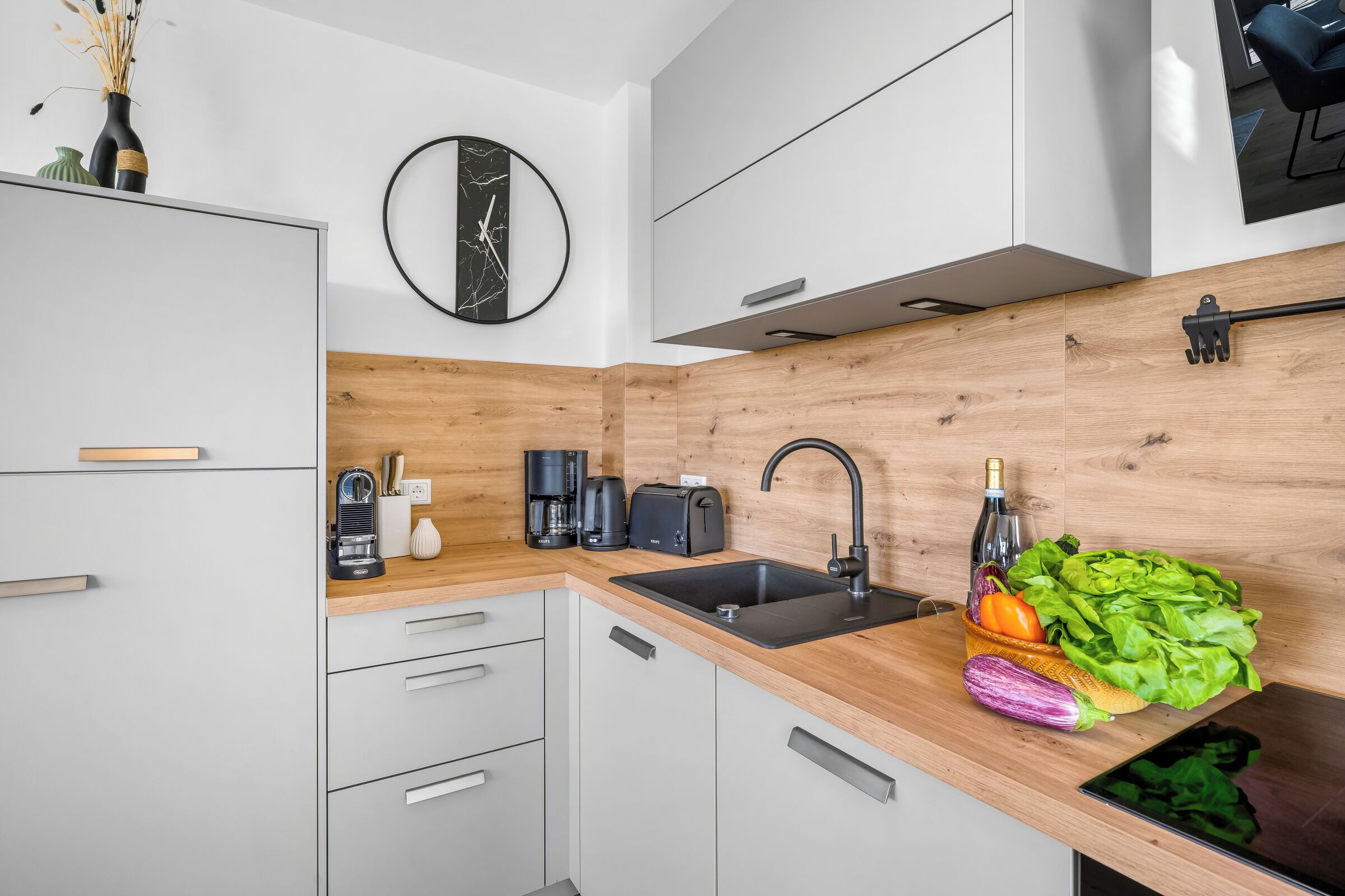 Eine moderne Küche mit Holzwandverkleidung, einem schwarzen Spülbecken und einer Kaffeemaschine.