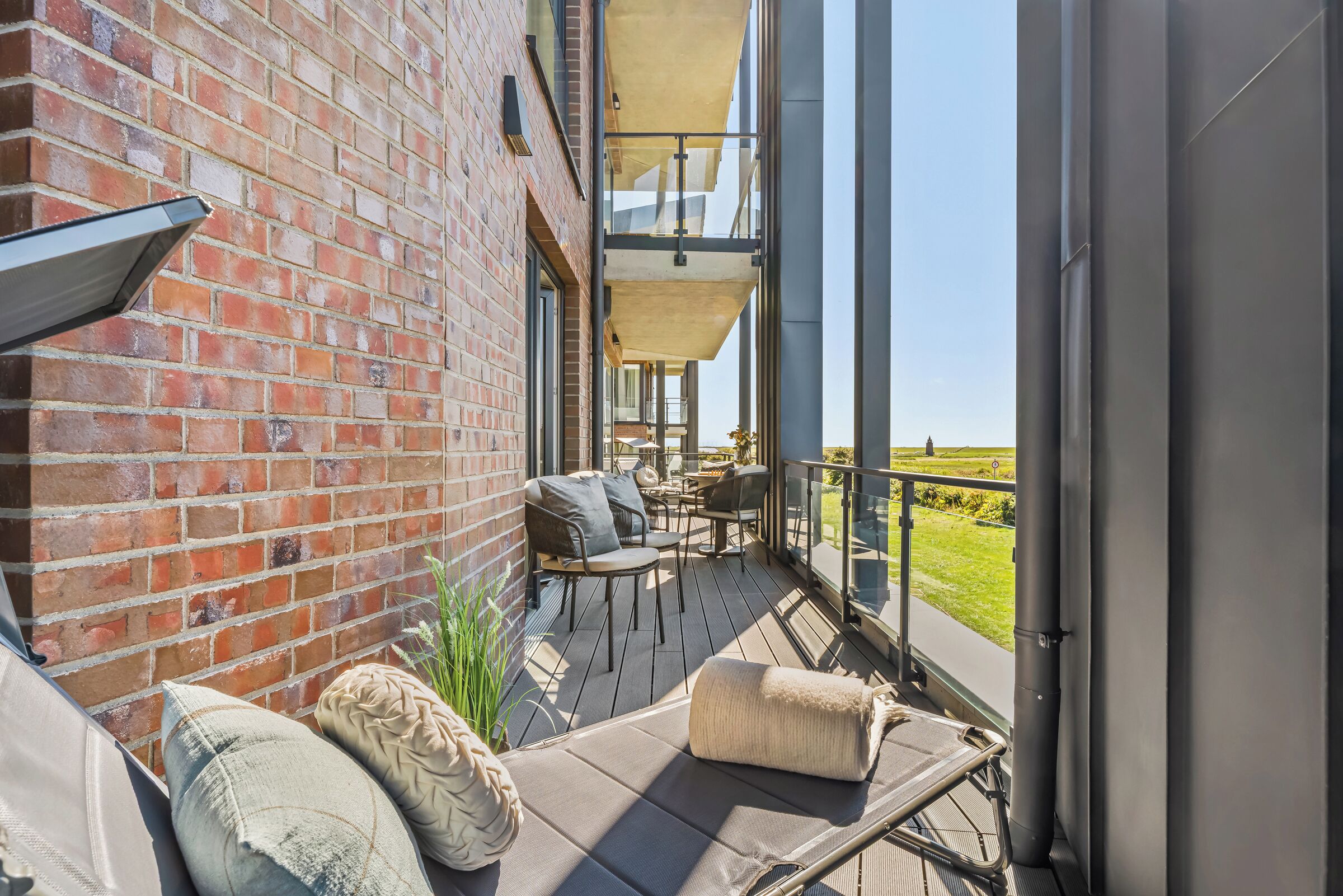 Ein Balkon mit Gartenmöbeln, einer Ziegelwand und Blick auf die Landschaft.
