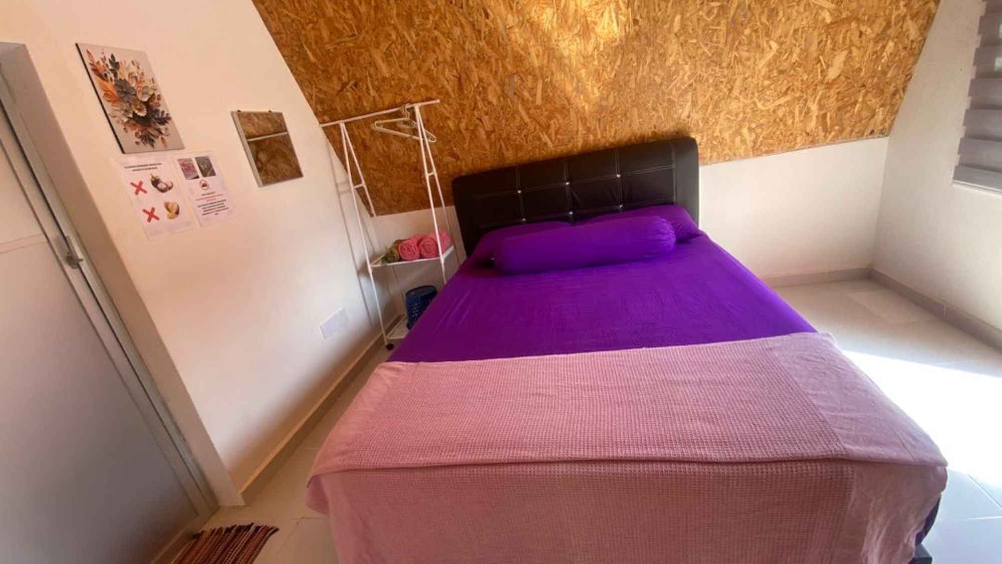 Une chambre à coucher avec un lit, une tête de lit en bois, un mur blanc et une petite étagère sur laquelle sont posés quelques objets.