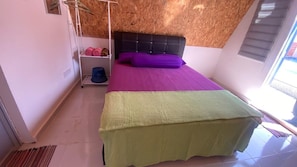 Un dormitorio con cama, estante con toallas dobladas y ventana.