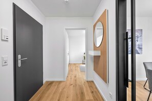 Un passadís modern amb una porta fosca, un panell de paret de fusta i una vista d'una altra habitació amb una planta.