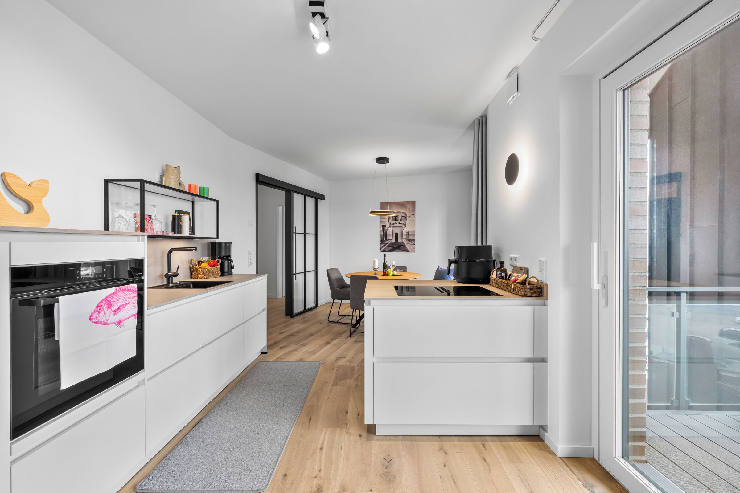 A modern kitchen with a built-in oven, a coffee machine, and a dining area with a table and chairs.