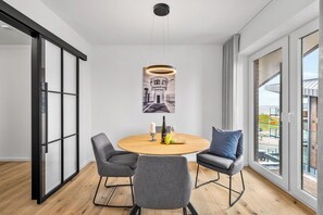 Een moderne eetruimte met een ronde tafel, vier grijze stoelen, een hanglamp en een ingelijste foto aan de muur.