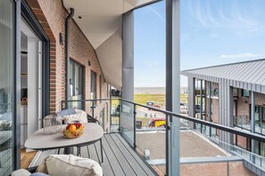 A balcony with a table, chairs, and a view of a train station. - The View B18 Hafenperle - Sea view, barbecue, shared. Sauna, car park (Dagebüll)