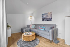 A modern living room with a grey sofa, a round wooden coffee table, and a floor lamp. - The View B18 Hafenperle - Sea view, barbecue, shared. Sauna, car park (Dagebüll)