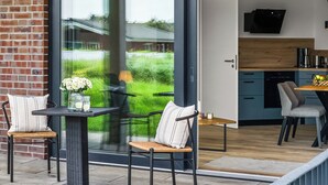 Eine moderne Außenpatio mit einer Ziegelwand, Schiebetüren und einem sichtbaren Küchenbereich durch die Türen hindurch.