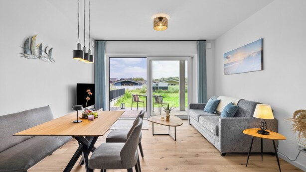 Ein modernes Wohnzimmer mit Essbereich, einer Couch, einem Couchtisch und Blick ins Freie.