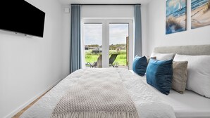 Ein Schlafzimmer mit einem Bett, einem Flachbildfernseher, einem großen Fenster und zwei Bildern.
