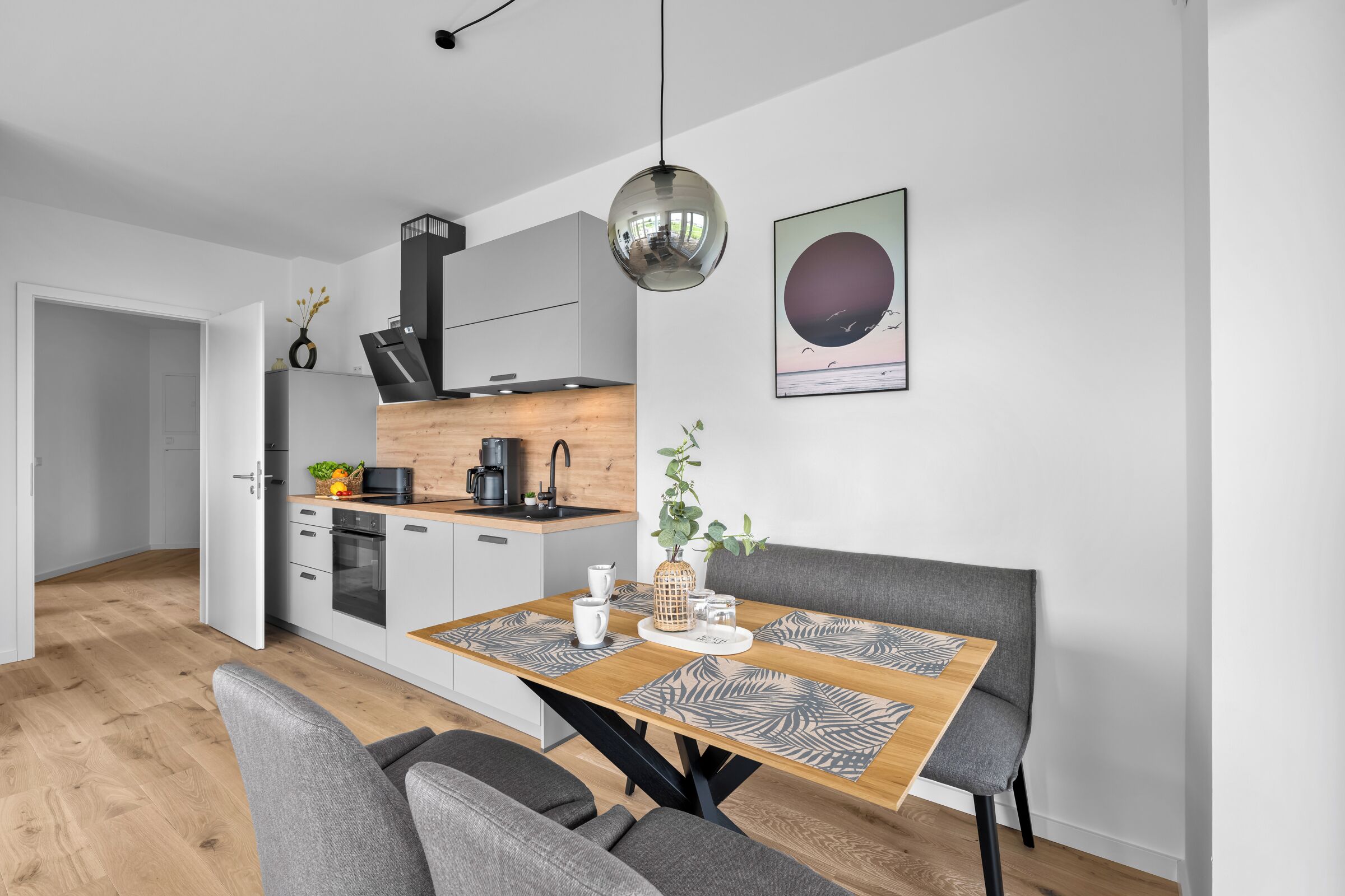 Een moderne keuken met een eetgedeelte, met een houten tafel, gestoffeerde grijze stoelen en een hanglamp.