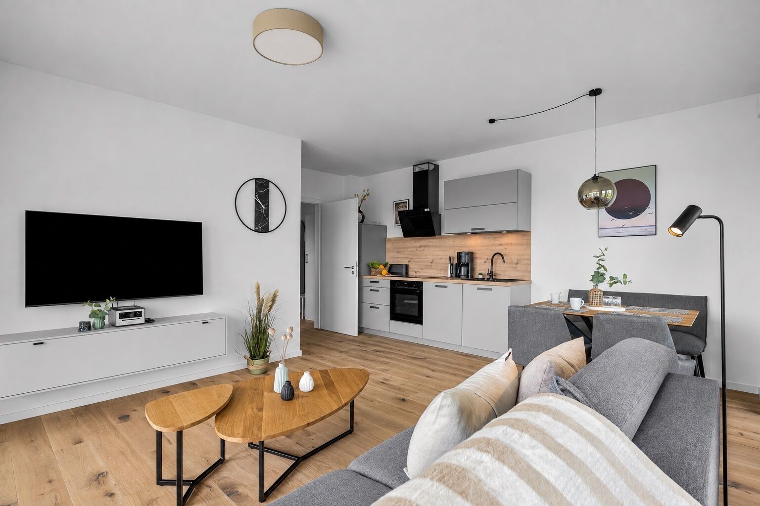 Ein modernes Wohnzimmer mit Flachbildfernseher, Couchtisch aus Holz und grauem Sofa.