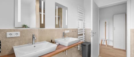 A modern bathroom with two sinks, a mirror, and a towel rack.