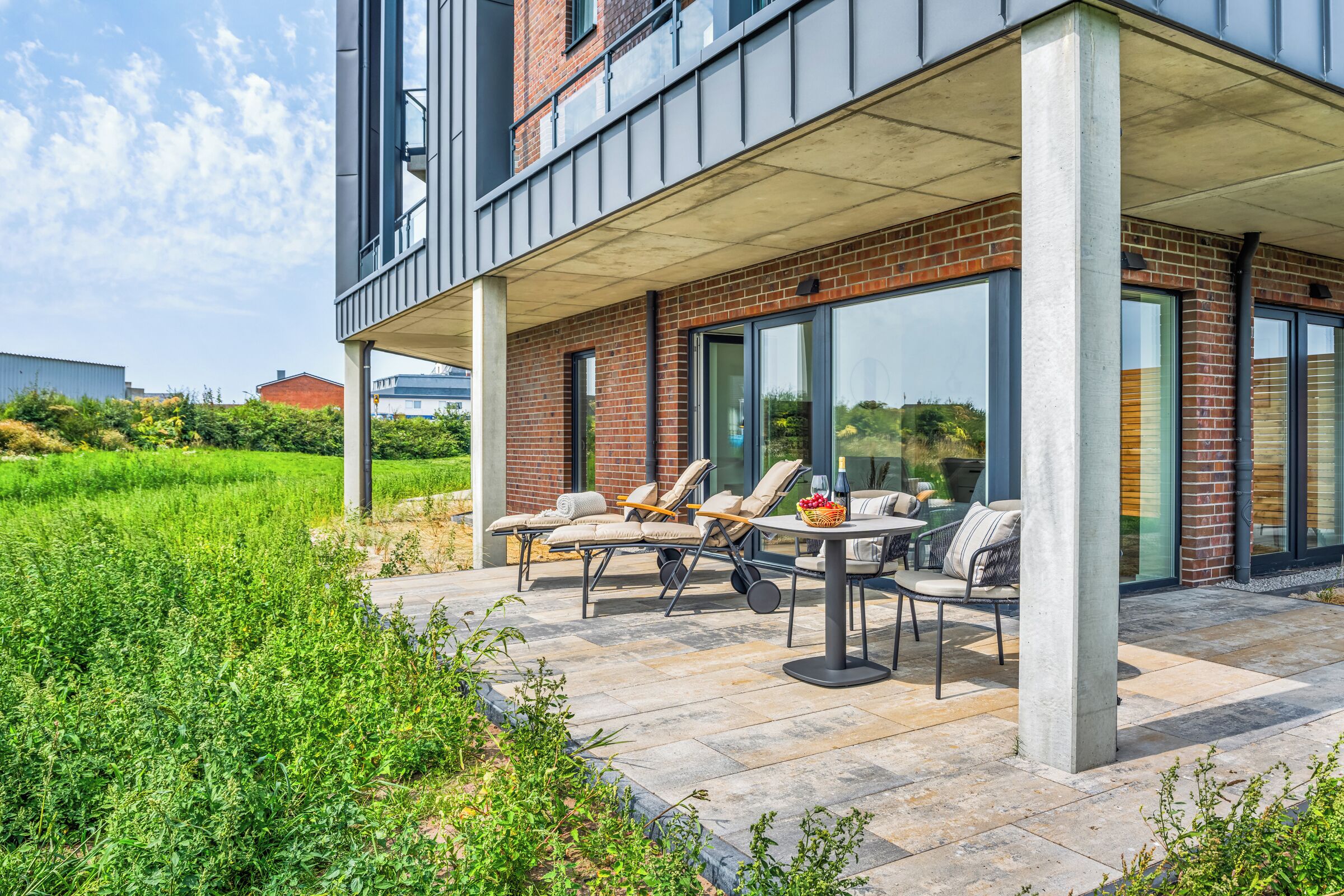 Un patio moderno al aire libre con un espacio de estar techado, una mesa y vista a un edificio de ladrillo.