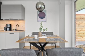 Eine moderne Küche mit Kaffeemaschine, einem hängenden Spiegel und einem gerahmten Kunstwerk über einem Esstisch mit einer Pflanze als Mittelstück.