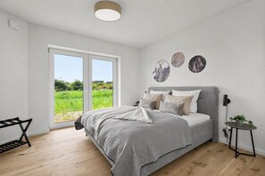 Ein Schlafzimmer mit Bett, Schreibtisch und Blick auf ein grünes Feld durch eine Schiebetür.
