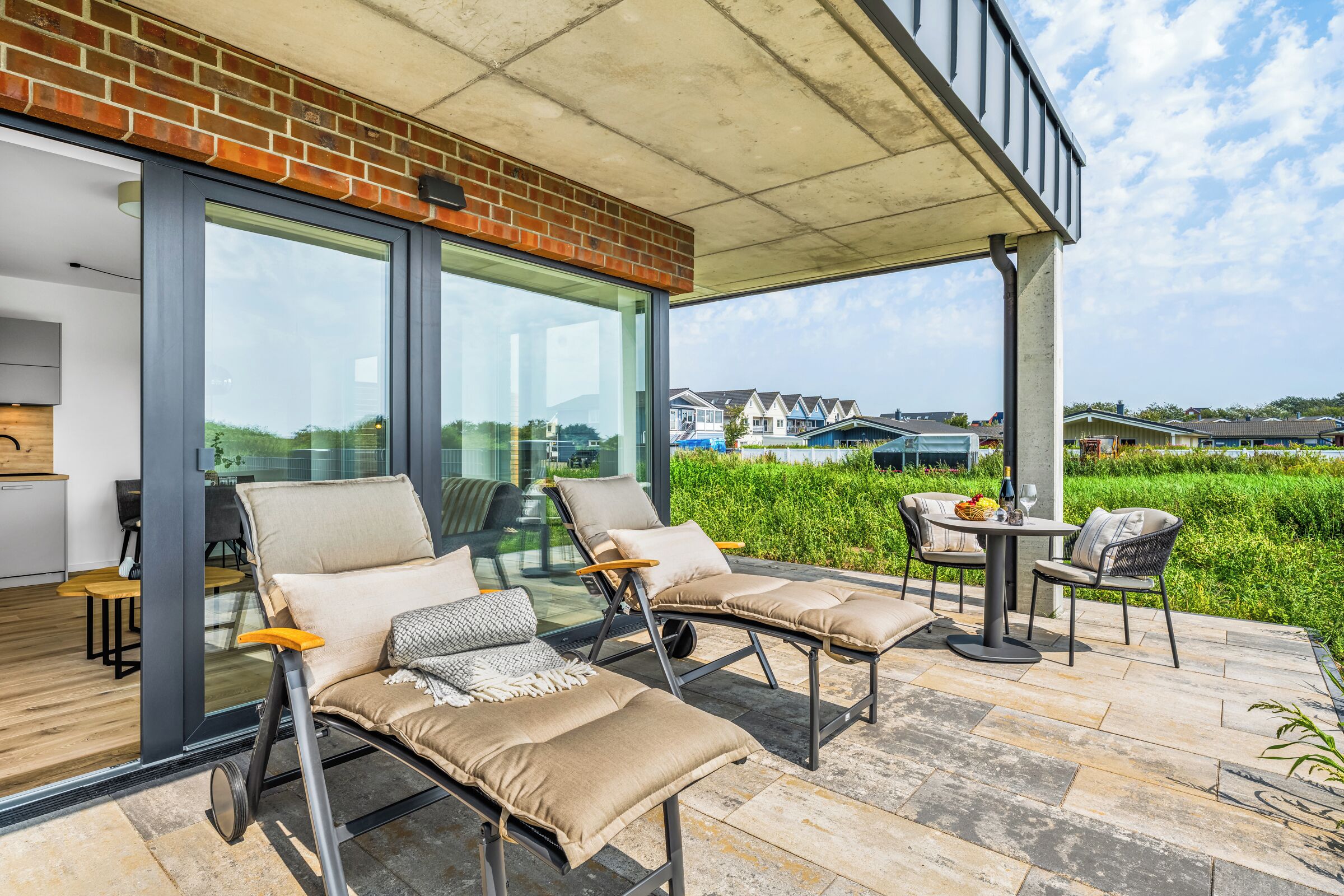 Eine moderne Außenlounge mit Glastüren zu einer Terrasse, ausgestattet mit Liegestühlen und einem Tisch.