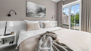 Une chambre moderne avec un grand lit, une table de chevet avec une lampe, un tableau accroché au mur et une vue sur l’extérieur grâce à une porte coulissante.