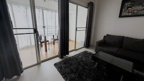 Una sala moderna con un sofá oscuro, una mesa de vidrio con sillas y vistas a un área exterior a través de grandes puertas correderas de vidrio.
