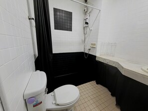 A bathroom with white tiled walls, a black bathtub, a white toilet, and a shower area. - Peaceful Pool-view Studio Near Jomtien Beach - Baan Suan Lalana (Pattaya)