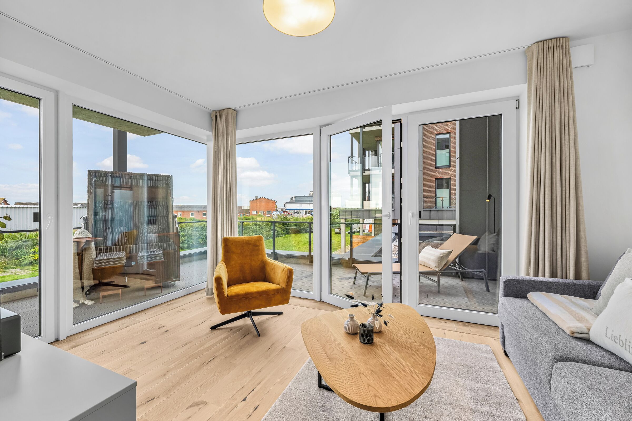 A spacious living area with a modern sofa, a wooden coffee table, and a comfortable armchair. Large glass doors lead to an outdoor balcony with a view of the city.