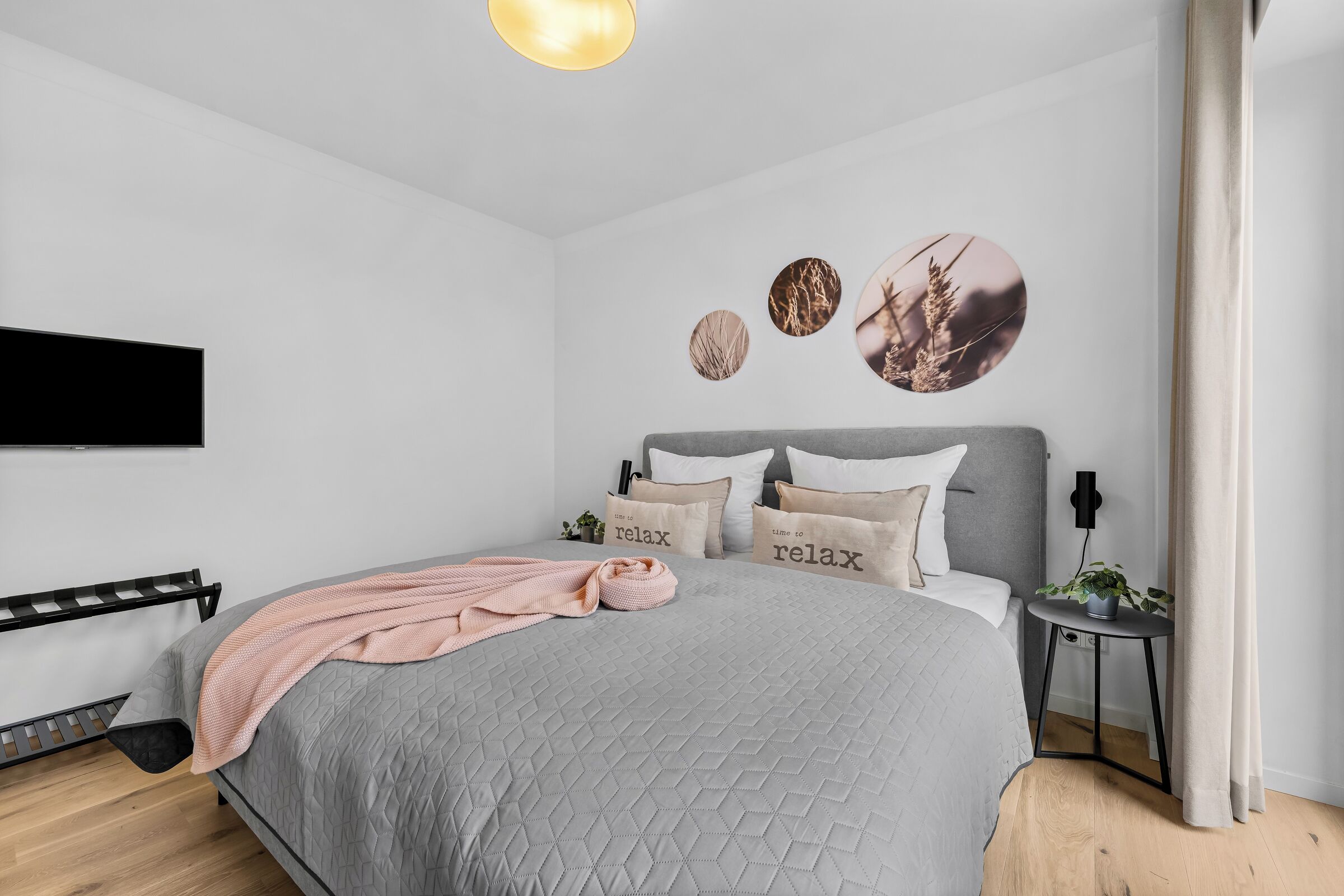 Une chambre à coucher moderne avec un lit, des oreillers, une table de chevet, un téléviseur fixé au mur et des œuvres d’art murales de forme circulaire.