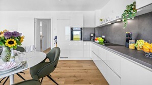 Eine moderne Küche mit weißen Schränken, einem eingebauten Backofen und einem Essbereich mit Tisch für zwei Personen.